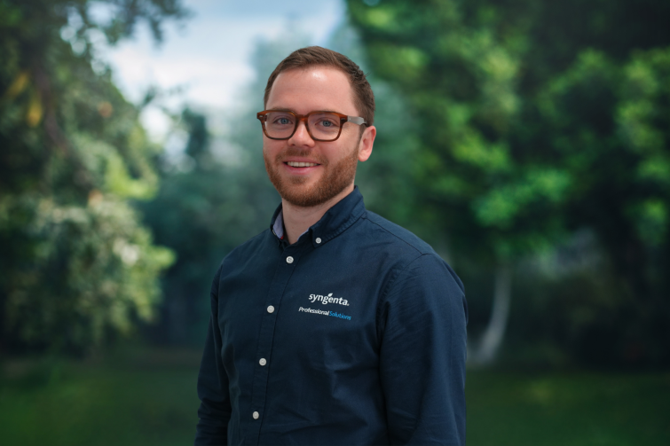 Smiling man in glasses wearing a dark button-up shirt in a green park