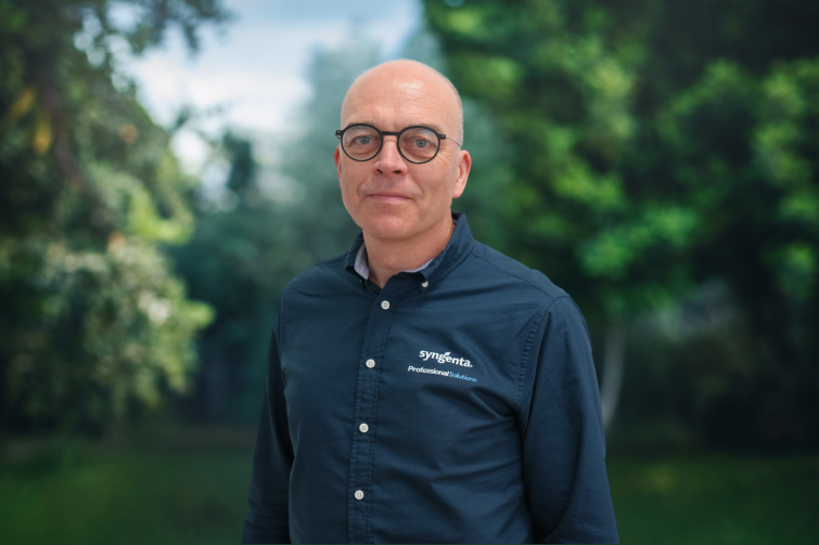 Smiling bald man in glasses wearing a dark button-up shirt outdoors in a park