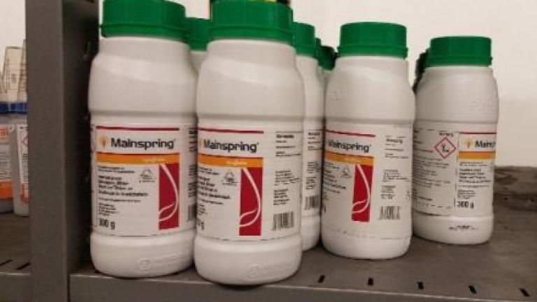 Four white chemical bottles with green caps on a metal shelf